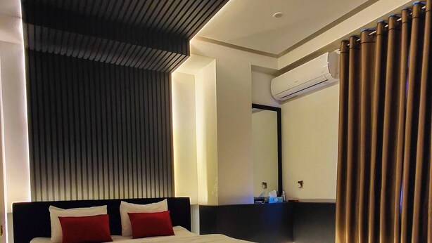 Een moderne hotelkamer met een groot bed, een donker hoofdeinde en een spiegel boven het bed.