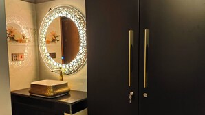 Een moderne badkamer met een donkere wastafel, een ronde spiegel met verlichting en een zwarte inloopkast.