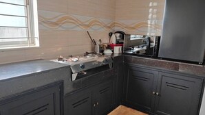 Een keuken met zwarte kastjes, een roestvrijstalen koelkast, een gasfornuis en een raam met zonwering.