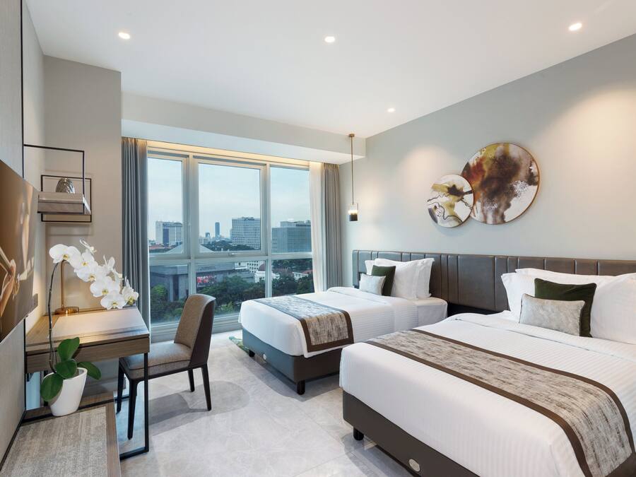 Una habitación de hotel moderna con dos camas, un escritorio y un ventanal con vistas a la ciudad.
