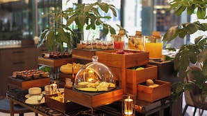 Een buffet met diverse gerechten en dranken, waaronder fruit, kazen en desserts, gepresenteerd op houten tafels met glazen potten.