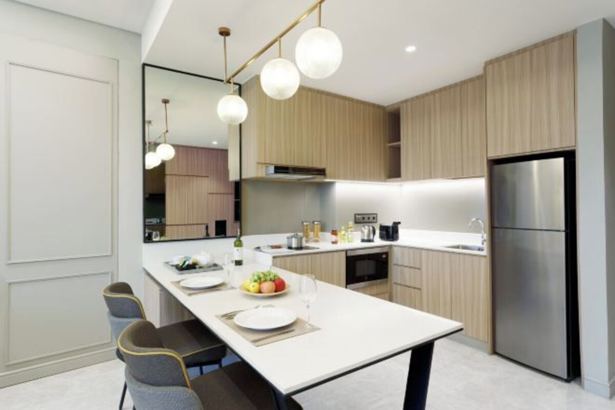 Une cuisine moderne dotée d’un îlot central, d’appareils électroménagers en acier inoxydable et de luminaires suspendus.