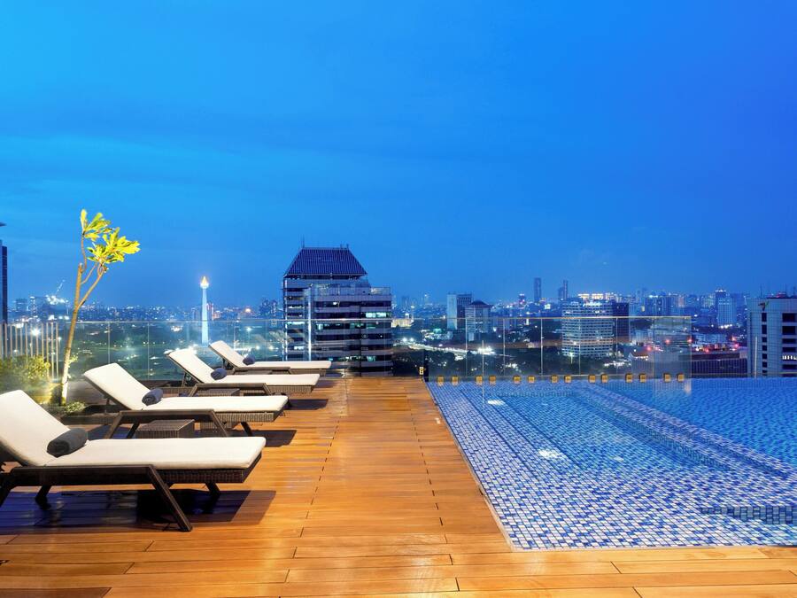 Un área de piscina en la azotea con sillones de descanso y vistas al horizonte de la ciudad al atardecer.