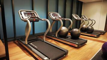 Varias cintas de correr con pantallas digitales, ubicadas en un gimnasio con suelo de madera y paredes azules.