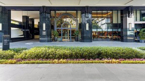 Een moderne hotelentree met een glazen gevel, een centraal portaal en een keurig onderhouden tuin ervoor.