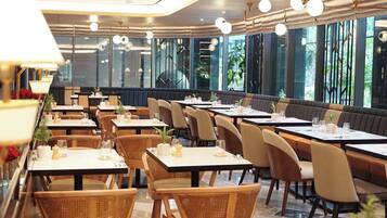 A restaurant with multiple tables and booths, large windows, and indoor plants.