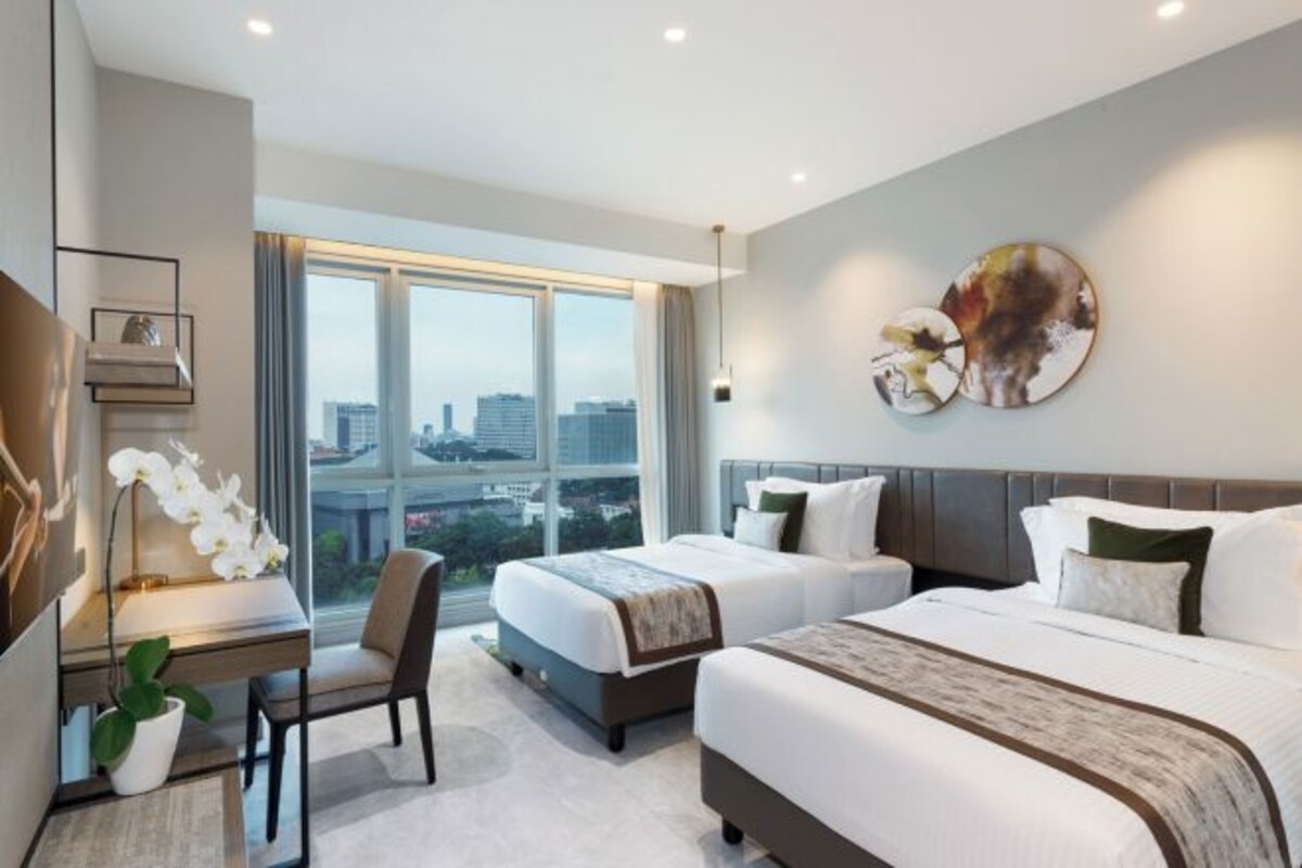 Une chambre d’hôtel moderne avec deux lits, un bureau et une grande fenêtre donnant sur la ville.