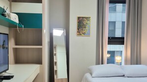 A hotel room with a bed, a desk with a computer and remote controls, a wardrobe, and a window with curtains. - 27 l Myeongdong 5min l Airport bus l Cozy Room (Seoul)
