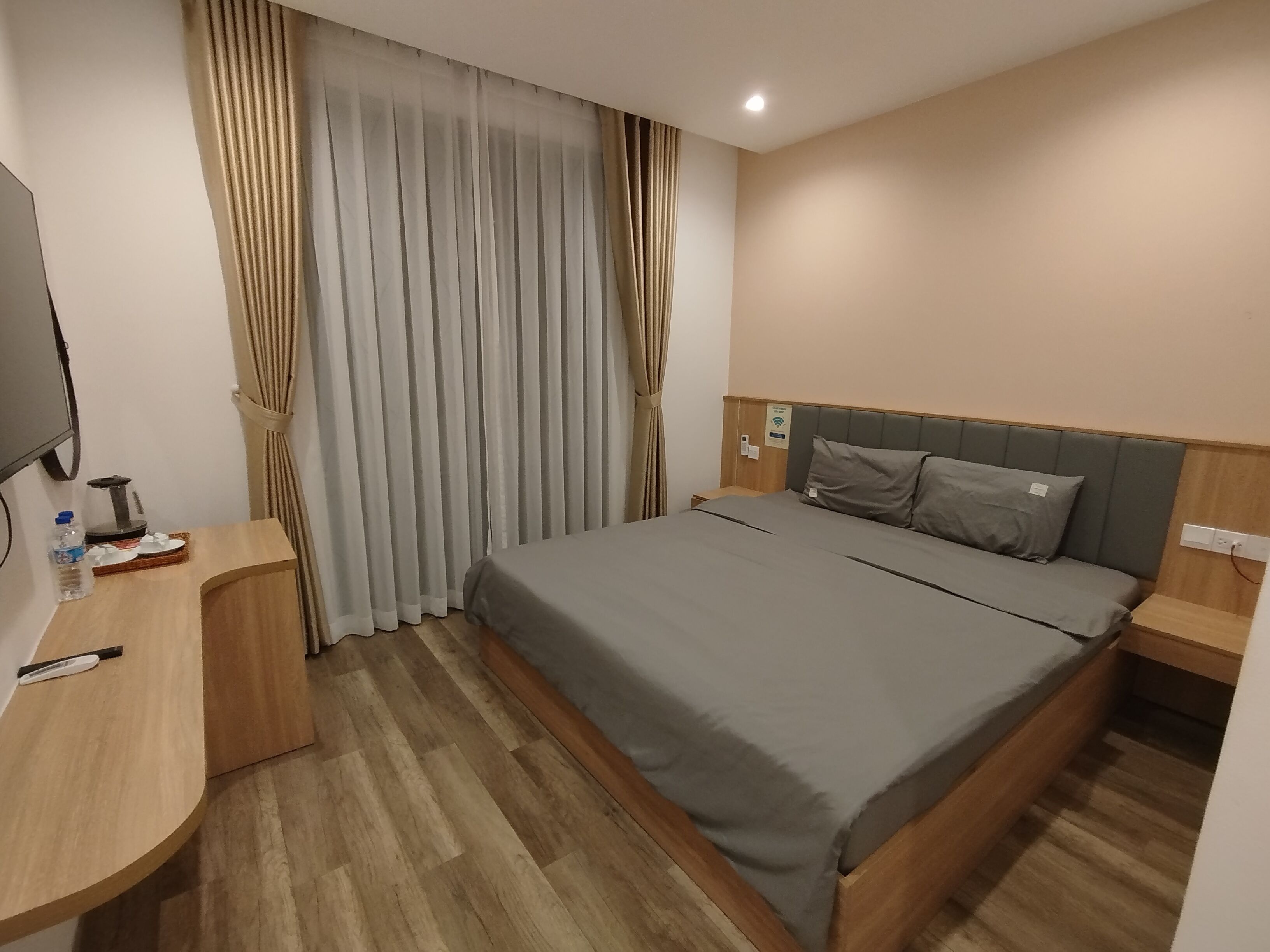 A hotel room with a bed, a desk, a chair, a TV, and a window with curtains.