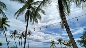 A pathway lined with palm trees and string lights leading to a beach area with umbrellas and lounge chairs. - Kalia Phu Quoc Hotel 2 (Phu Quoc)