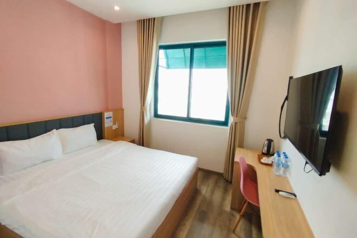 Una camera d'albergo con un letto, una scrivania con sedia, una televisione e una finestra con tende.