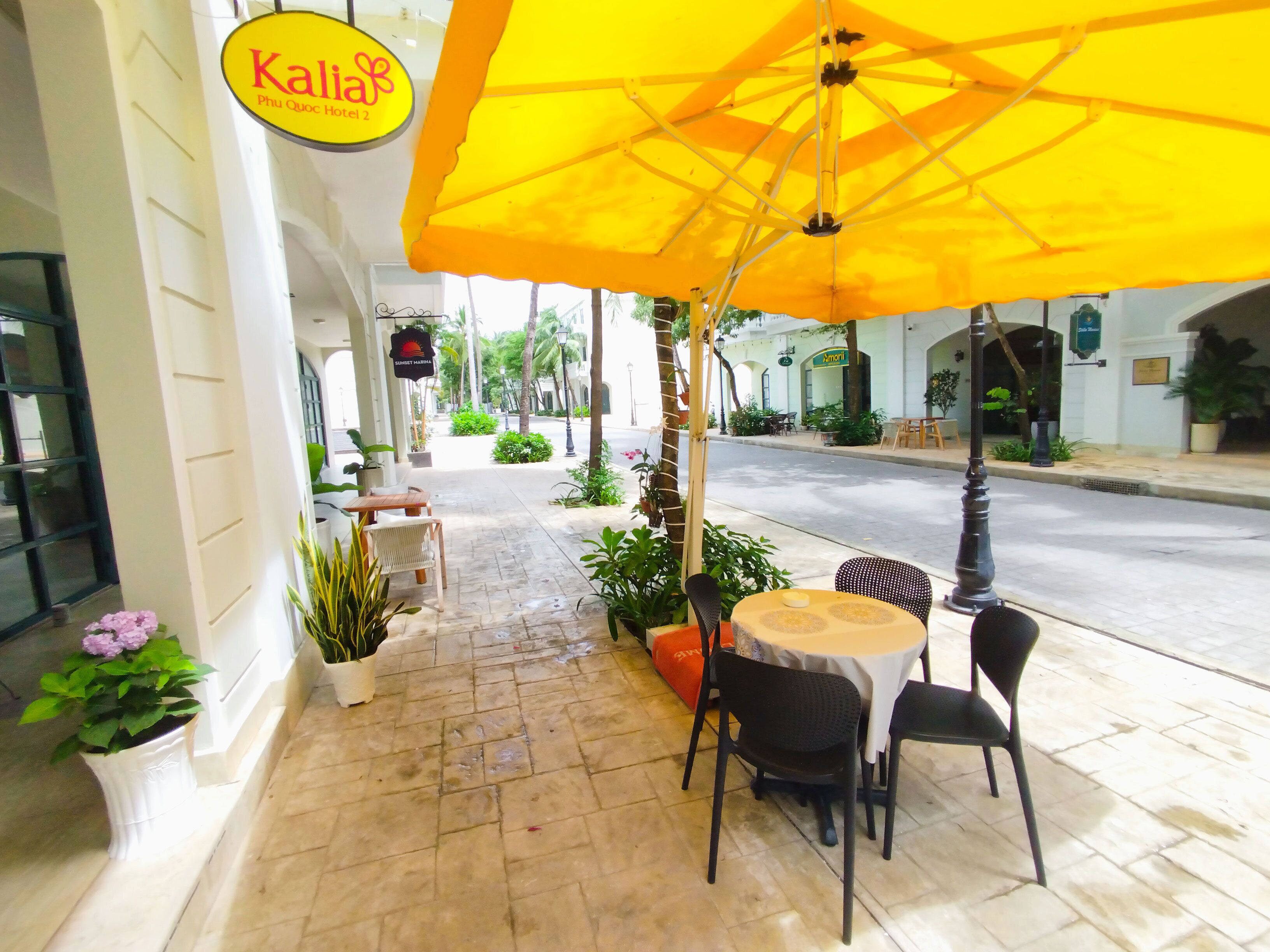 An outdoor seating area with a yellow umbrella, potted plants, and a sign for Kallia Phu Quoc Hotel 2.