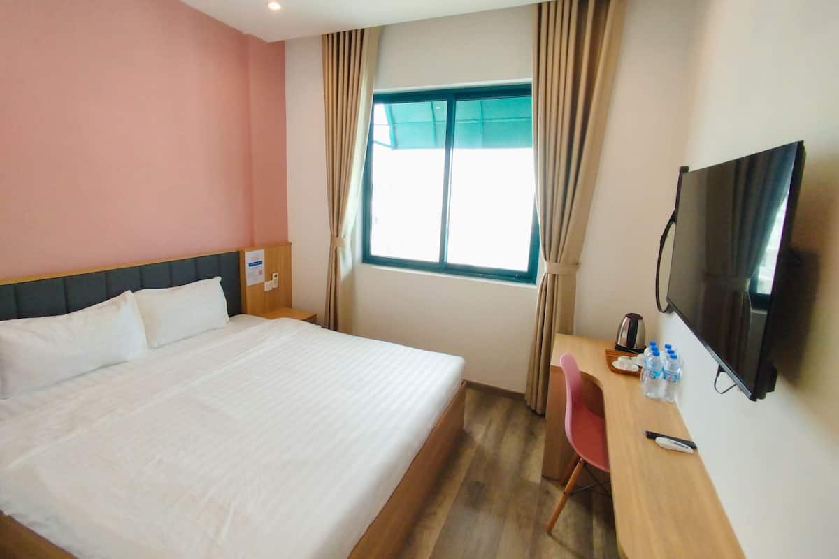 Una camera d'albergo con un letto, una scrivania con sedia, una televisione e una finestra con tende.