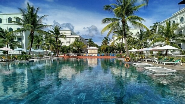 A large swimming pool with clear blue water, surrounded by palm trees and sun loungers. - Kalia Phu Quoc Hotel 2 (Phu Quoc)