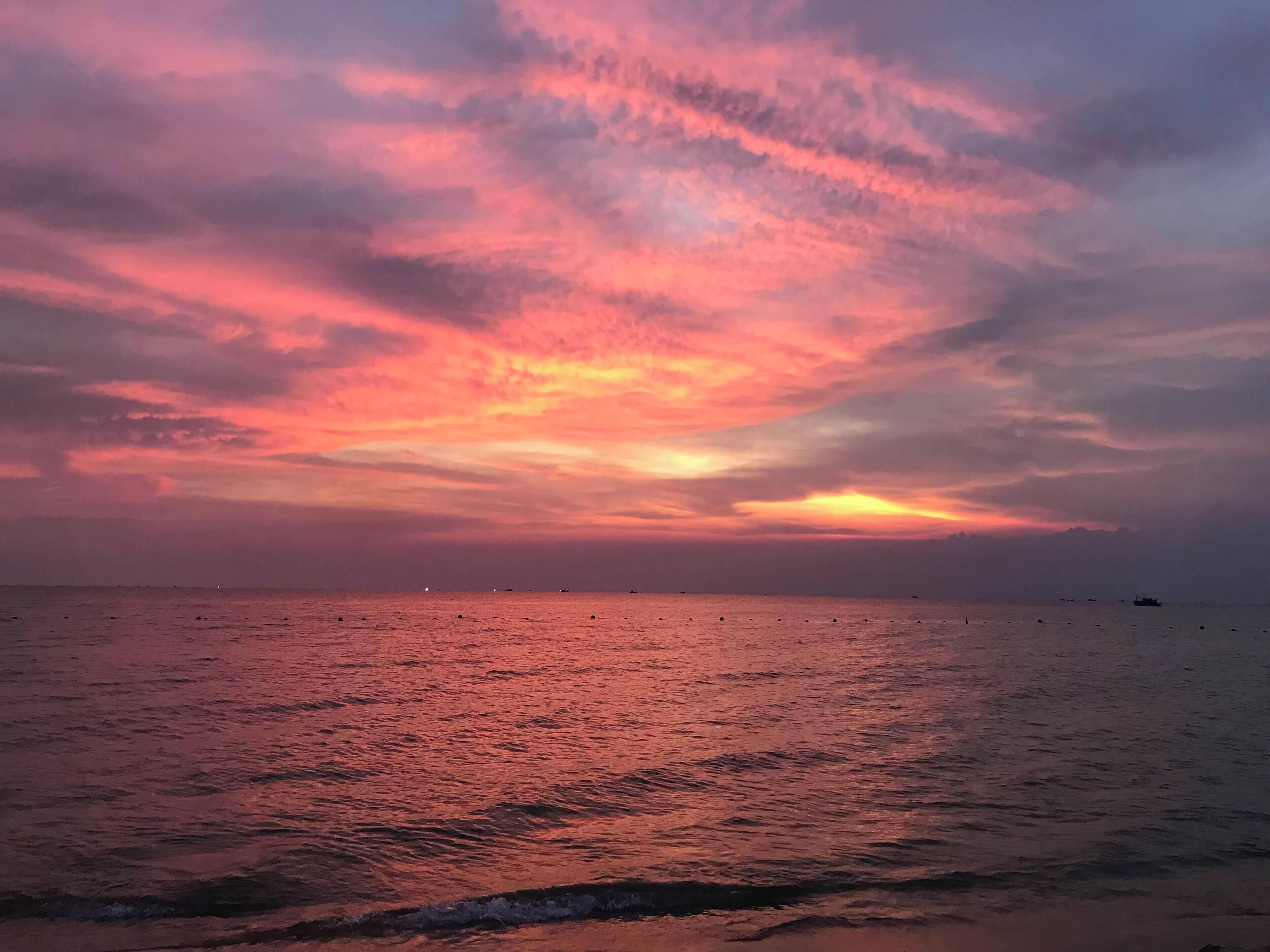 Un atardecer sobre un mar tranquilo con barcos a lo lejos.