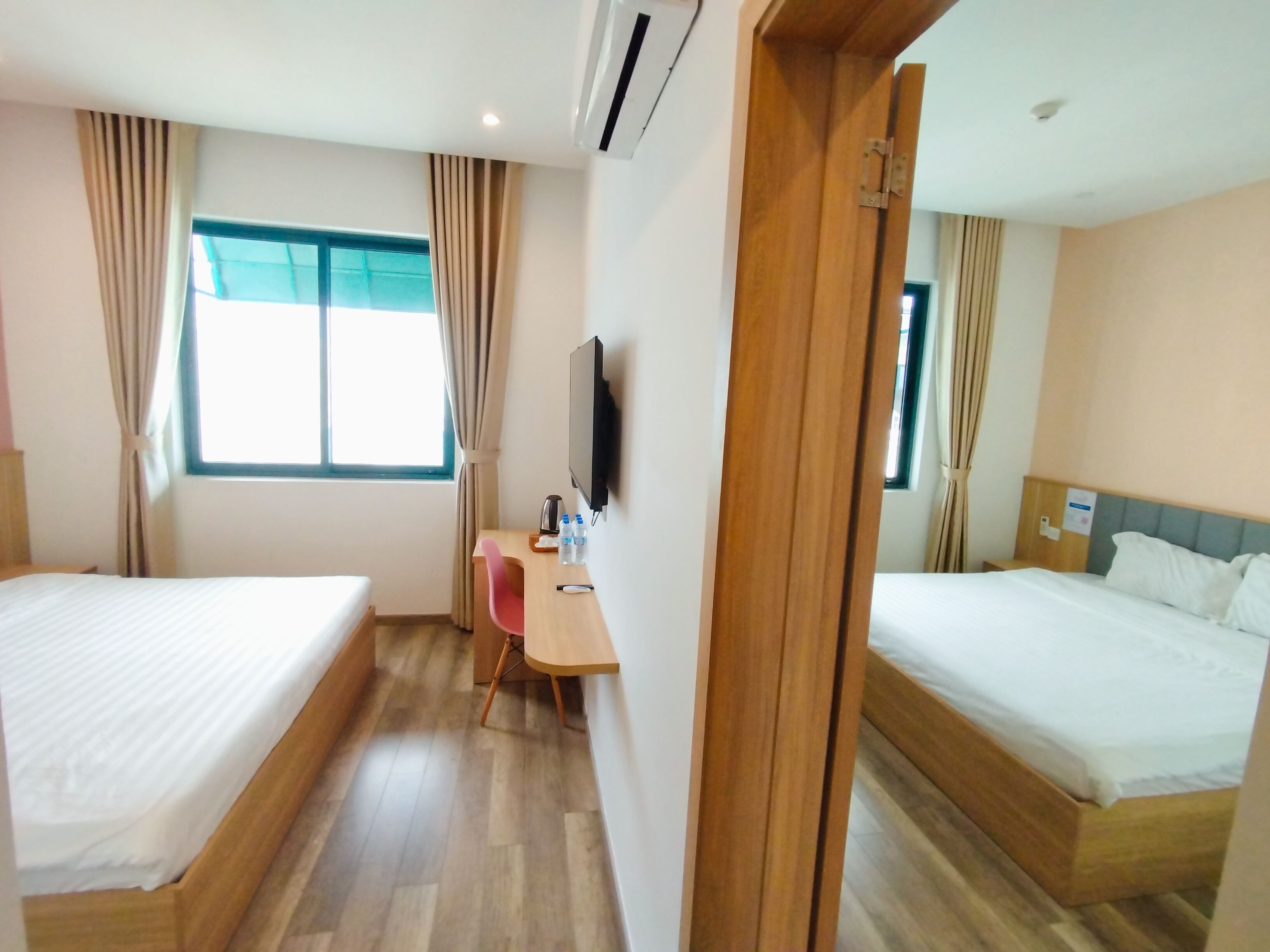A hotel room with two beds, a desk with a chair, a television, and a window with curtains.