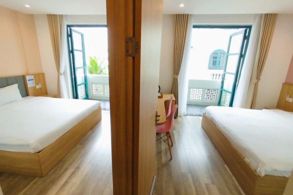 Quarto de hotel com duas camas, uma escrivaninha e vista para o exterior.