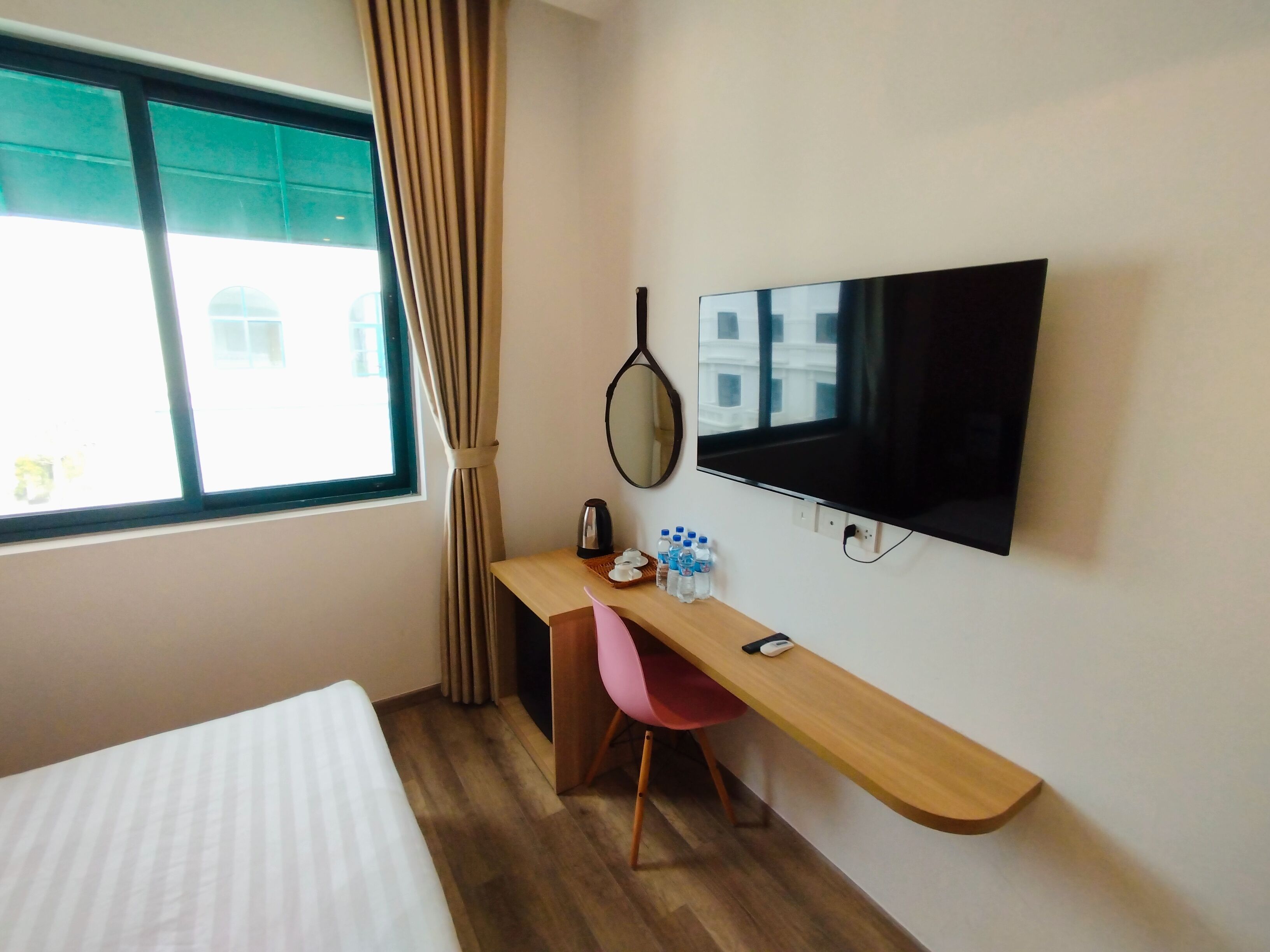 Ein Hotelzimmer mit Bett, Schreibtisch mit Stuhl, Fernseher, Fenster mit Vorhängen und Spiegel.