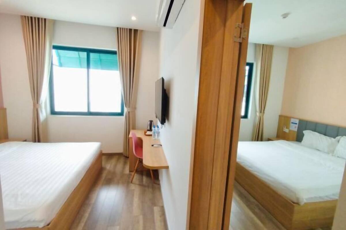 Camera d'albergo con due letti, una scrivania, una sedia, una televisione e una finestra con tende.