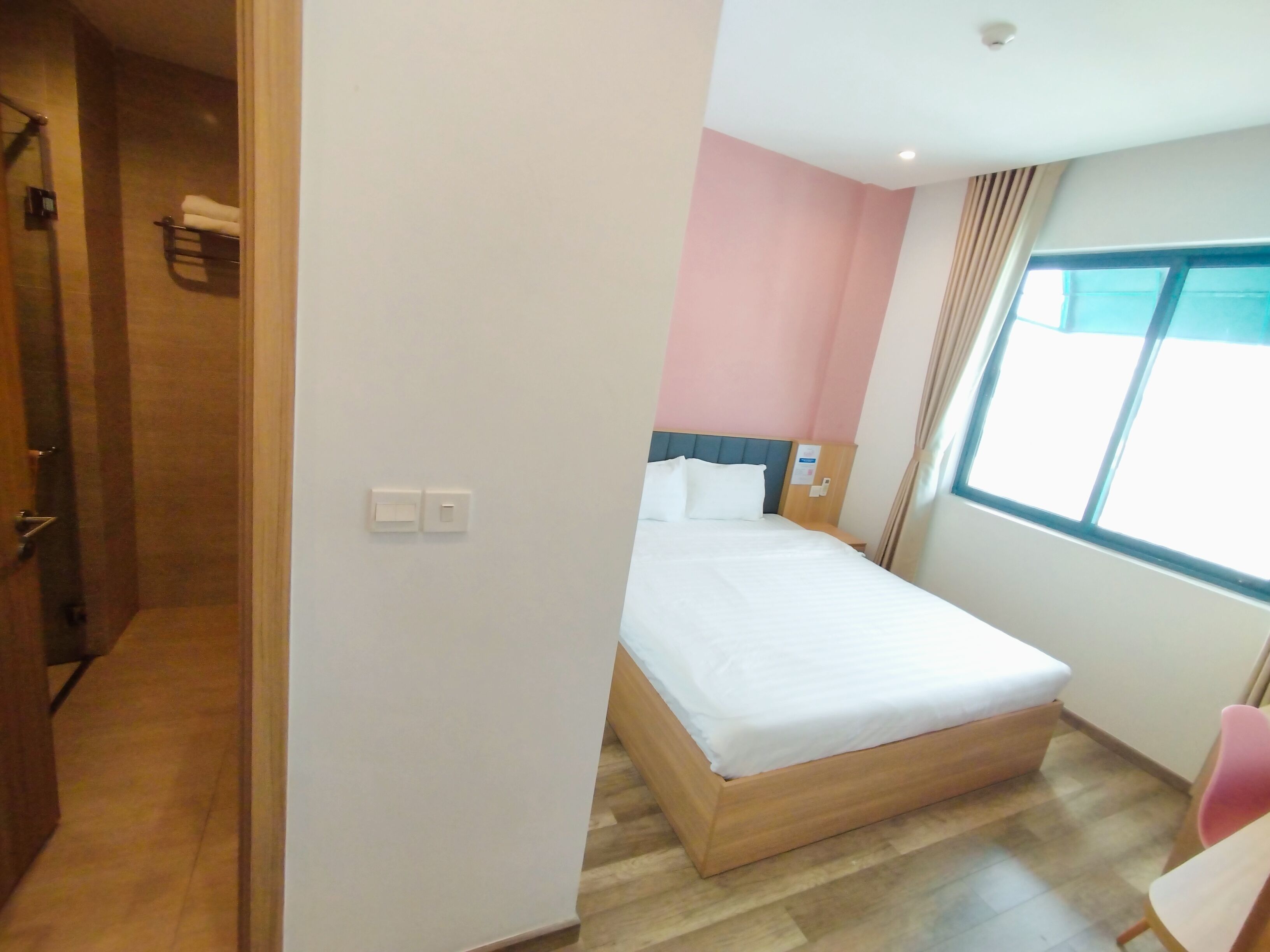 A hotel room with a wooden bed, a window with curtains, and a door leading to a bathroom.