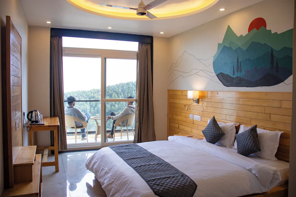 A hotel room with a large bed, a wooden headboard, a view of the outdoors, and a dining area with a table and chairs.