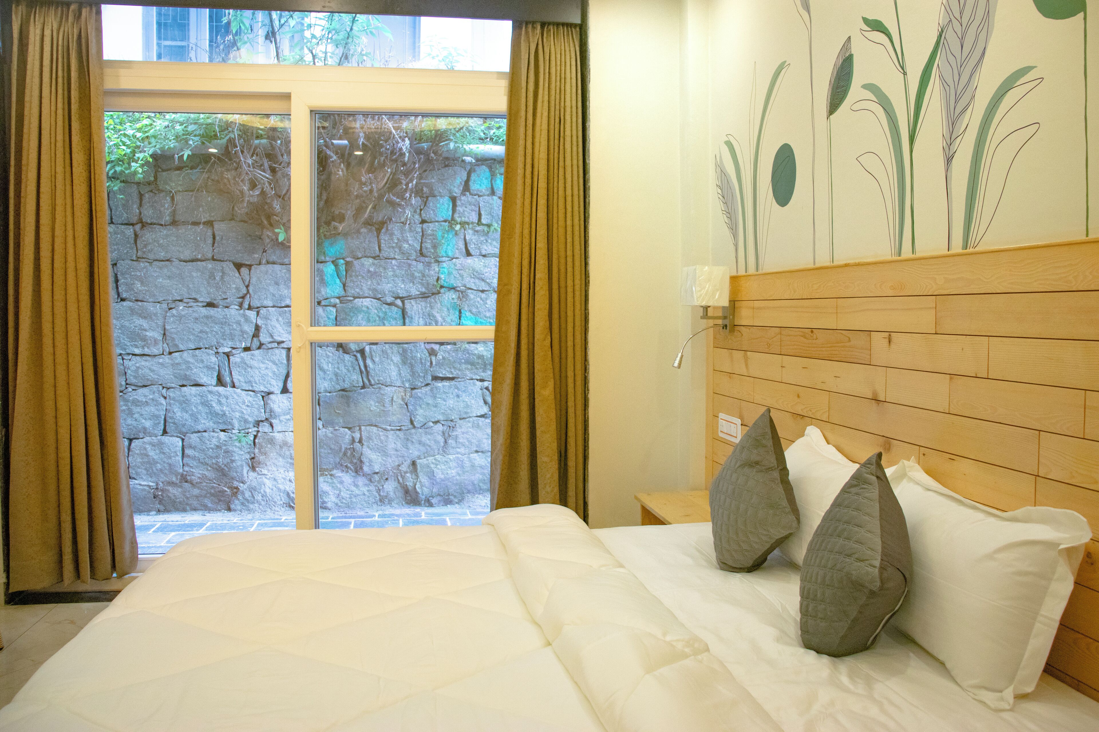 Ein Schlafzimmer mit Steinsandsteinwand, Holz-Kopfteil und einem Bett mit weißer Bettwäsche und grauen Kissen.