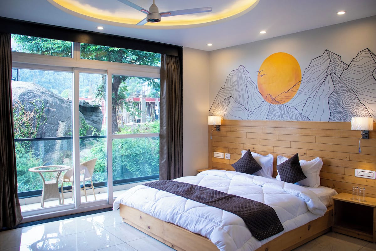 A bedroom with a large bed, a view of greenery through the window, and a wall mural.
