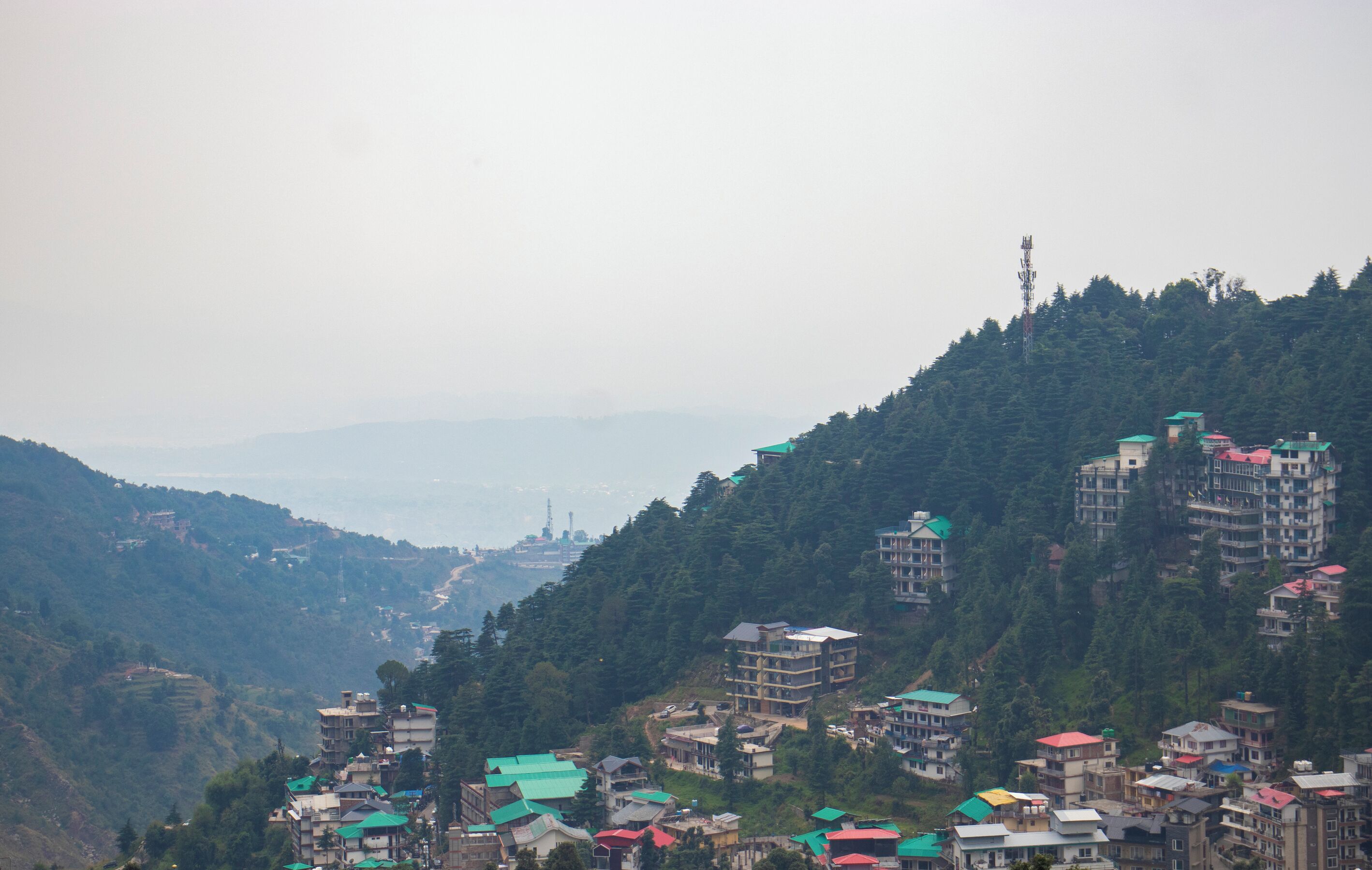 Un village perché sur une colline, avec des bâtiments à plusieurs étages, des champs en terrasses et une vue lointaine sur une ville.