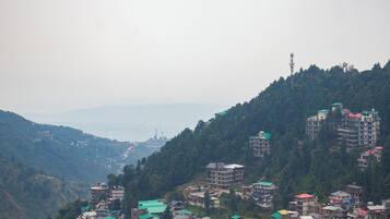 Un village perché sur une colline, avec des bâtiments à plusieurs étages, des champs en terrasses et une vue lointaine sur une ville.