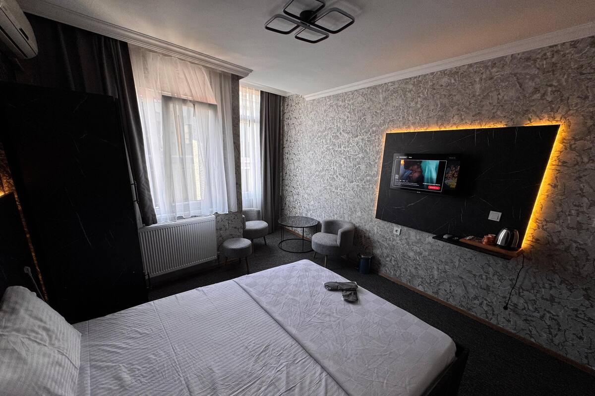 Habitación de hotel con una cama grande, un televisor en la pared, una mesita redonda y una silla.