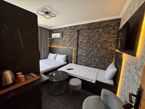 Una habitación de hotel con dos camas, una mesita redonda pequeña, una cafetera y un televisor montado en la pared.