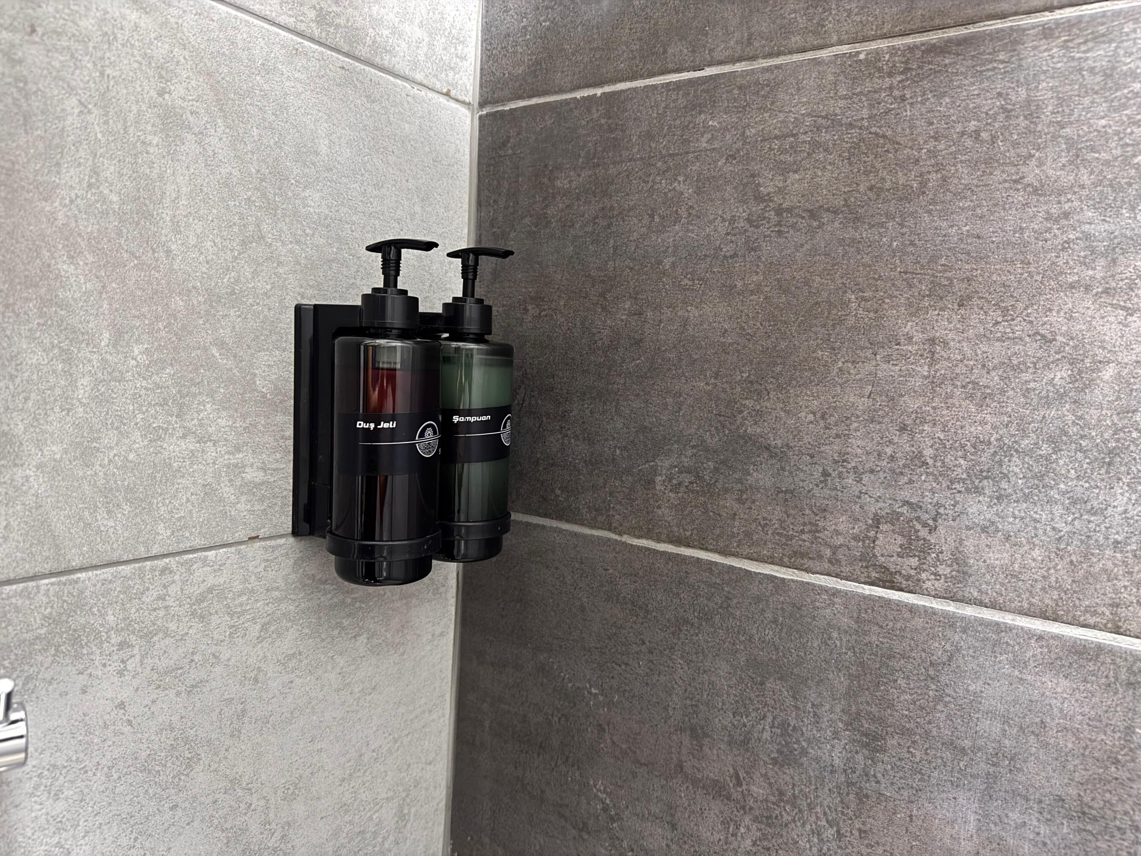 A bathroom with grey tiles and two black dispensers mounted on the wall.