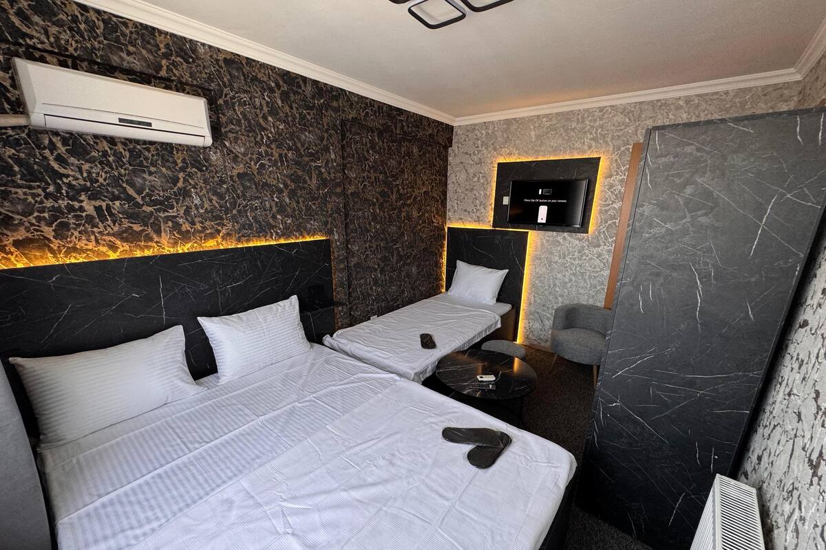 Habitación de hotel con dos camas, un televisor montado en la pared y un diseño moderno con texturas en las paredes que imitan el mármol.