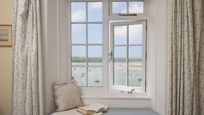 Een kamer met erker en uitzicht op een waterpartij met boten, een comfortabele bank en een boek.
