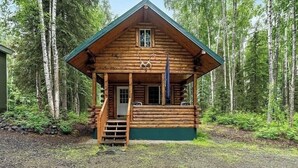 En træhytte med veranda, omgivet af skov.
