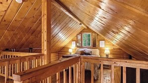 Et hyggeligt soveværelse i skunken med trælofter, en seng, et vindue og et lille bord med lampe.