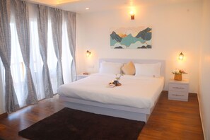Un dormitorio con una cama grande, dos mesitas de noche, un cuadro colgado en la pared y una ventana con cortinas.