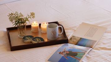 A tray with candles, a mug, and a glass vase with flowers on a bed.