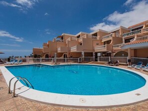 Un hotel con piscina, varios balcones y un cielo azul despejado.