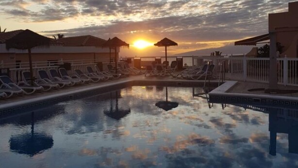 A pool with lounge chairs and umbrellas, reflecting the sunset.