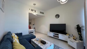 Un salon moderne avec un canapé bleu foncé, une table basse blanche et un téléviseur à écran plat posé sur un meuble TV blanc.