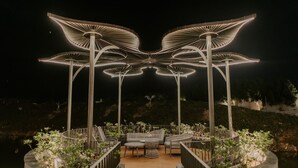 An outdoor seating area with tables and chairs, surrounded by planters and illuminated by large, circular light fixtures. - Floating deck resort  (Bhuj)