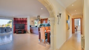 A spacious living area with a TV, dining table, and chairs, a kitchen with wooden cabinets, and a view of the outdoors. - Spectacular villa with private pool and sea views in Denia (Denia)