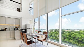 A modern kitchen with a large window, a dining area with a table and chairs, and a view of greenery outside. - Galena by Kozystay - Alam Sutera (South Tangerang)