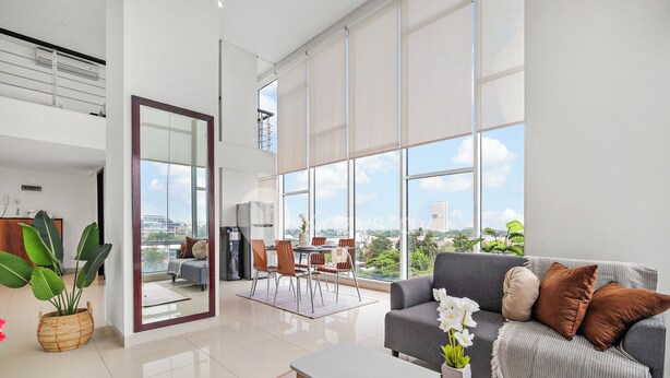 A modern living room with a grey sofa, a coffee table, and a dining area with chairs and a table. - Galena by Kozystay - Alam Sutera (South Tangerang)