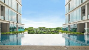 A modern hotel with a large infinity pool, surrounded by lush greenery and a clear blue sky. - Galena by Kozystay - Alam Sutera (South Tangerang)