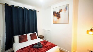 Ein Hotelzimmer mit Bett, dunklen Vorhängen, einem Bild an der Wand, einem Nachttisch und einer Lampe.
