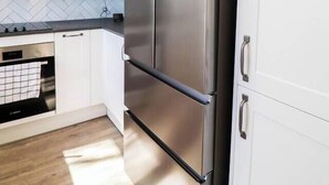Une cuisine moderne avec des meubles blancs, un réfrigérateur en acier inoxydable et un dosseret orné d’un motif en chevrons.