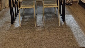 Un coin repas avec une table et des chaises, de grandes fenêtres donnant sur un paysage verdoyant et une commode blanche.