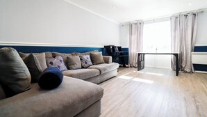 Un salon moderne avec un canapé d’angle, une petite table et une bibliothèque.
